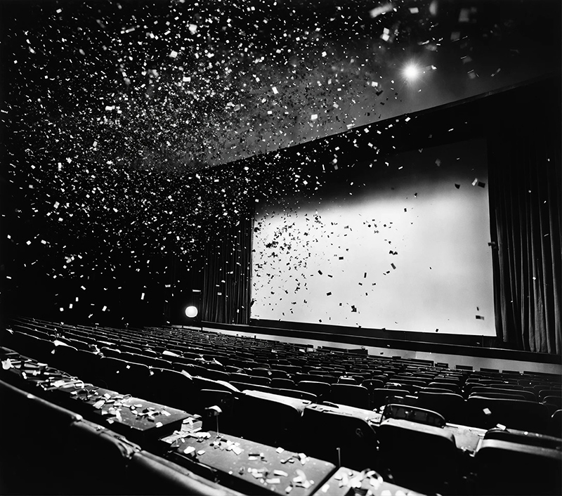 Photo noir et blanc d'une salle de cinéma, des confettis sont projetés sur les sièges vides.