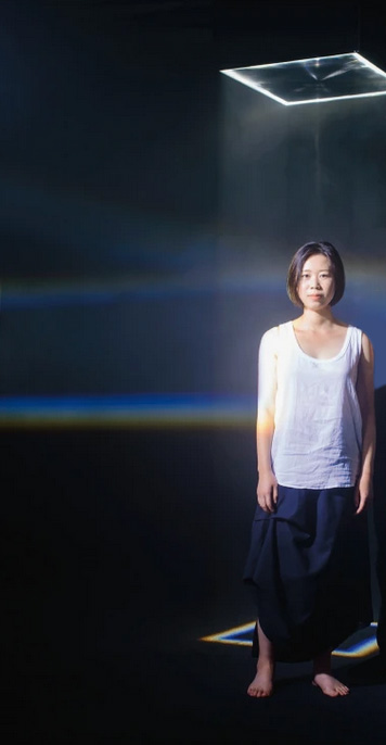 Photo de Jingfang Hao sur un fond très sombre avec une projection d'un carré lumière sur le sol